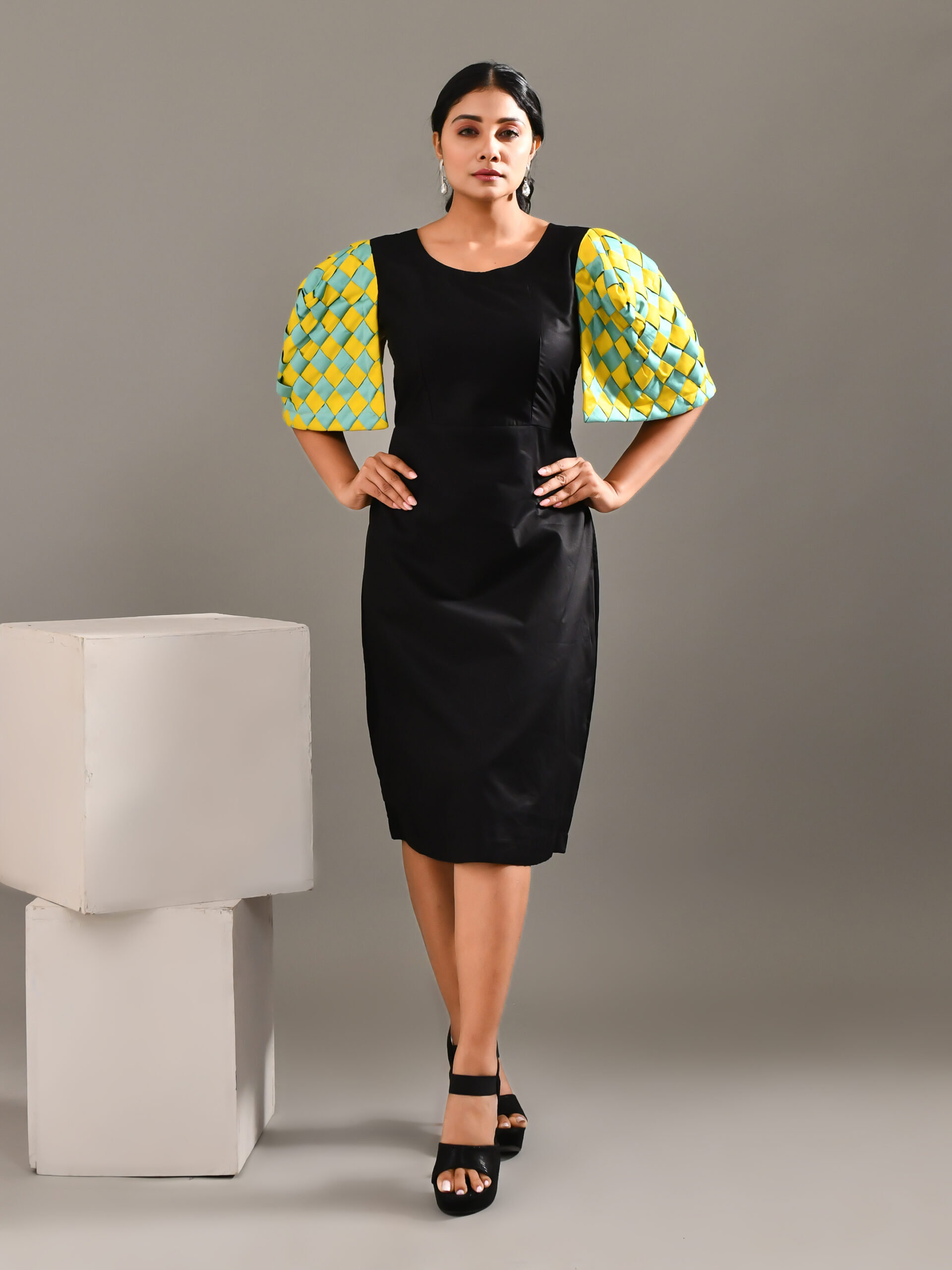 “Golden Muslin black cotton dress with bold exaggerated sculpted shoulders and intertwined vibrant sleeve detailing.”