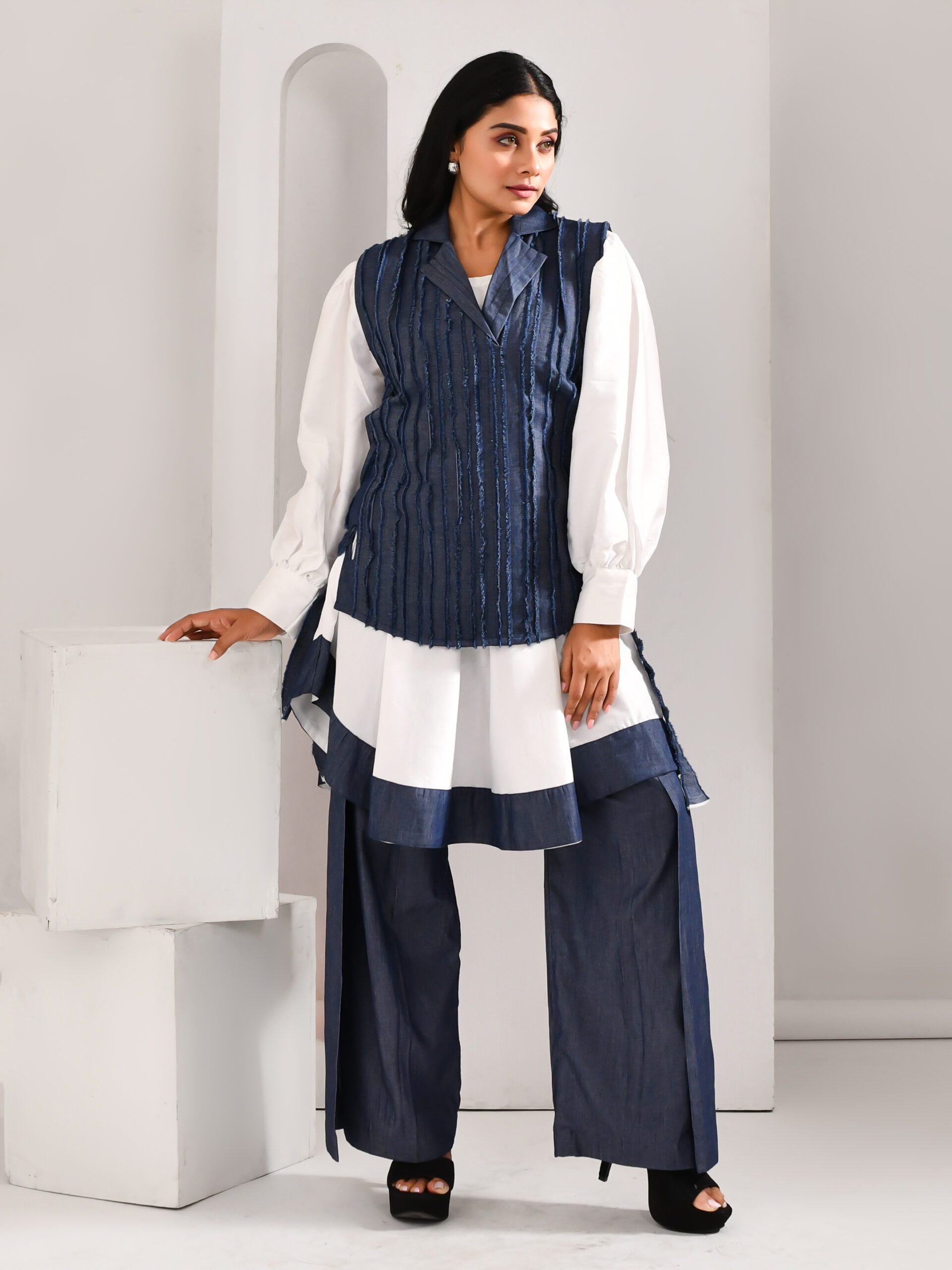 “Golden Muslin white and denim blue blended cotton and organza three-piece co-ord set with flat pants, high-low textured shirt, and tie-up jacket featuring denim-inspired detailing.”