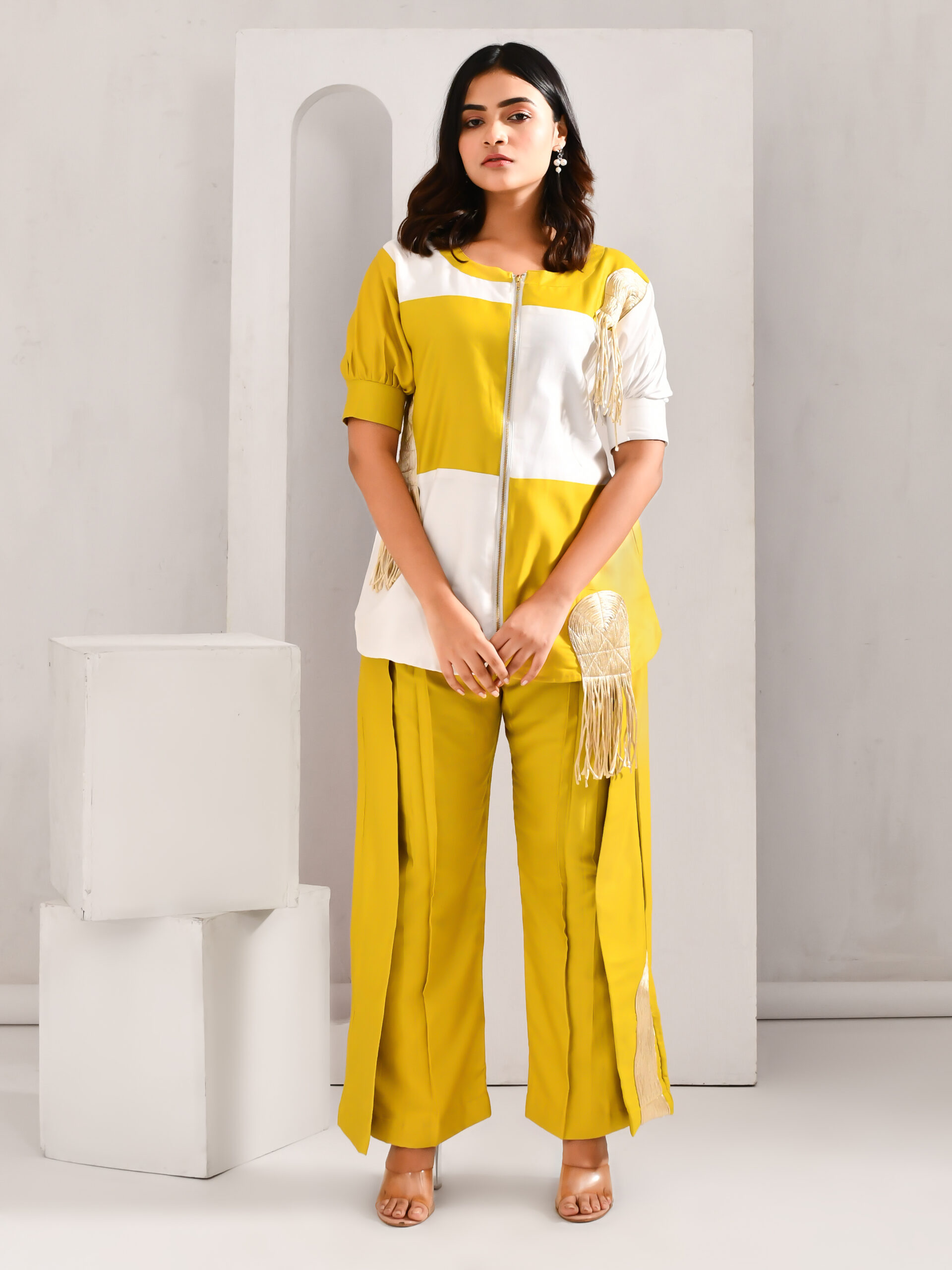 “Golden Muslin greenish yellow and white blended cotton co-ord set with tasselled top, golden appliques, and front zipper, paired with matching pants.”