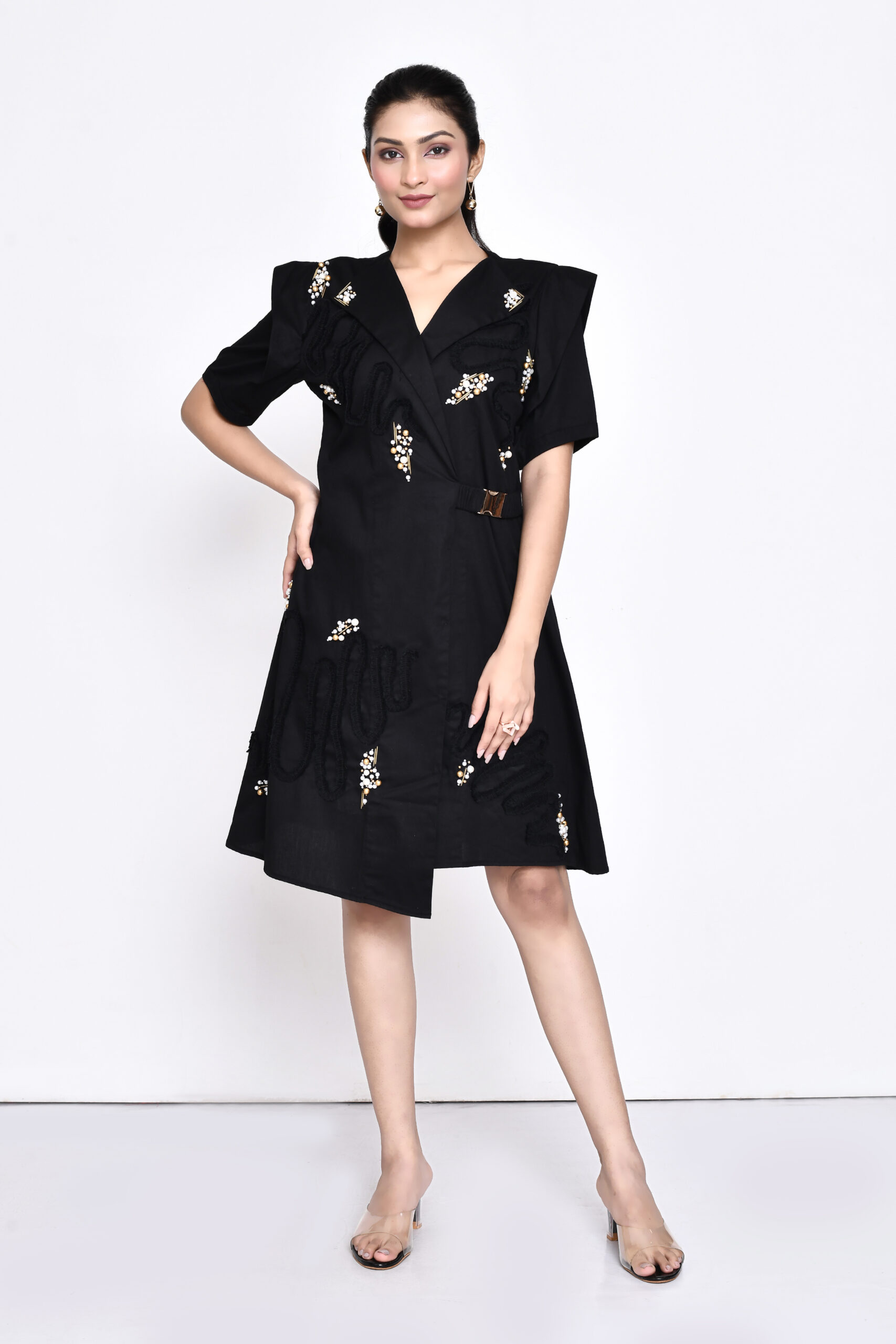 Golden Muslin black poplin overlap dress with lapel collar, embellished sleeves, fabric ruching, pearls, and gold waist buckle