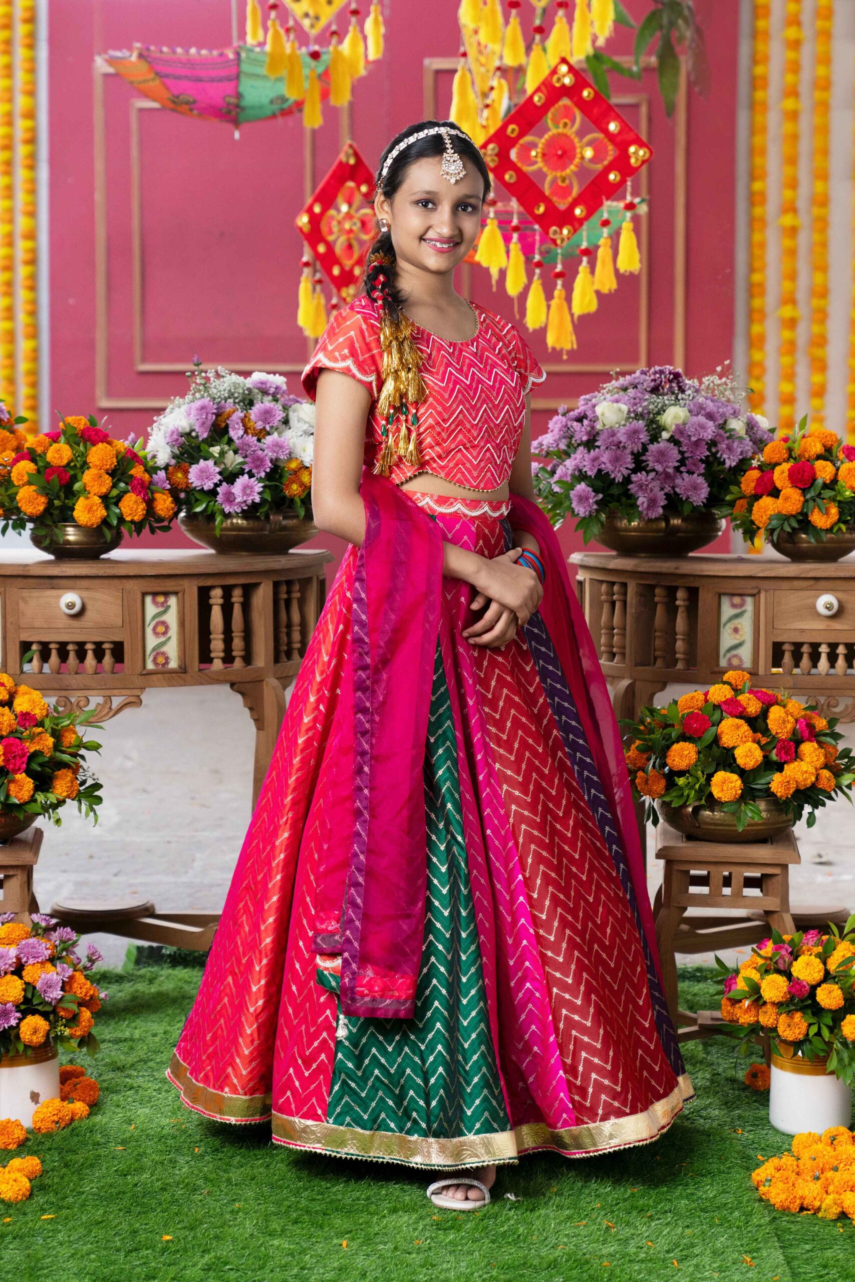 Presenting a multi-colored lehenga set featuring vibrant red fitted crop top in silk and organza adorned with golden chevron embroidery. The round neckline and cap sleeves are highlighted with golden piping