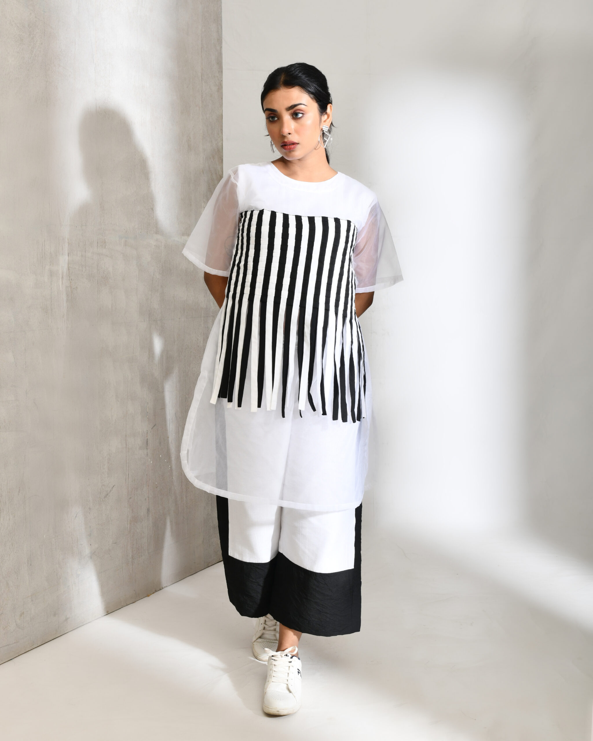 “Golden Muslin black and white blended cotton and organza co-ord set with sheer textured stripe top and high-waisted straight-leg color-blocked pants.”