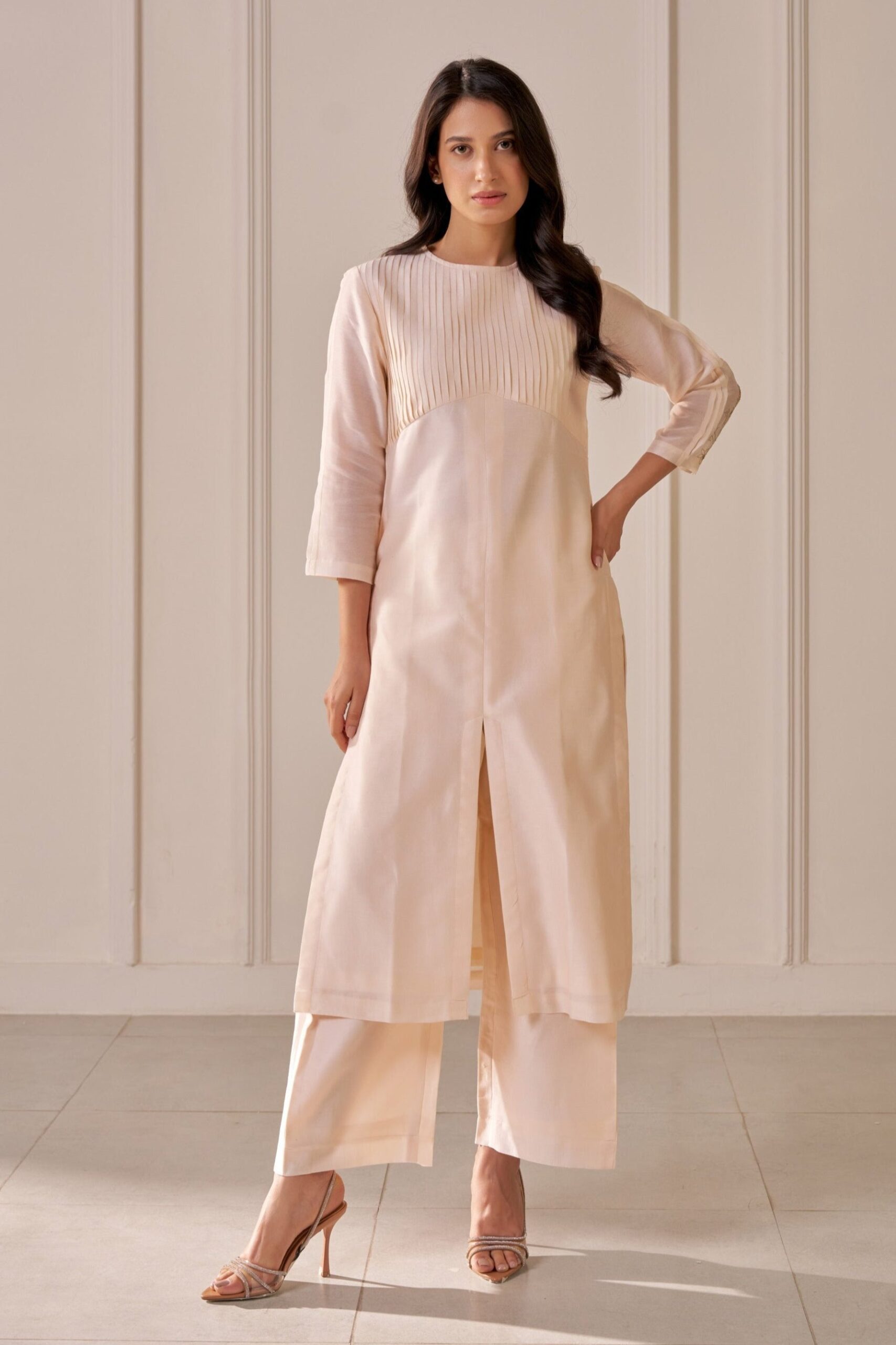 “Golden Muslin soft peach kurta with zari Tuberose embroidery and spaced tucks, paired with soft peach Chanderi wide-leg pants featuring side pleat detailing.”