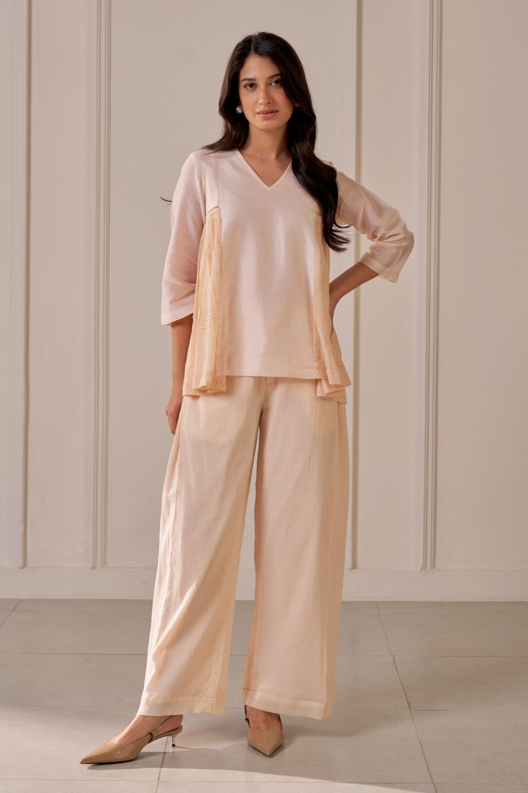 “Golden Muslin soft peach Chanderi top with V-neck and pleated crepe printed side panels, paired with matching crepe cotton wide-leg pleated pants.”