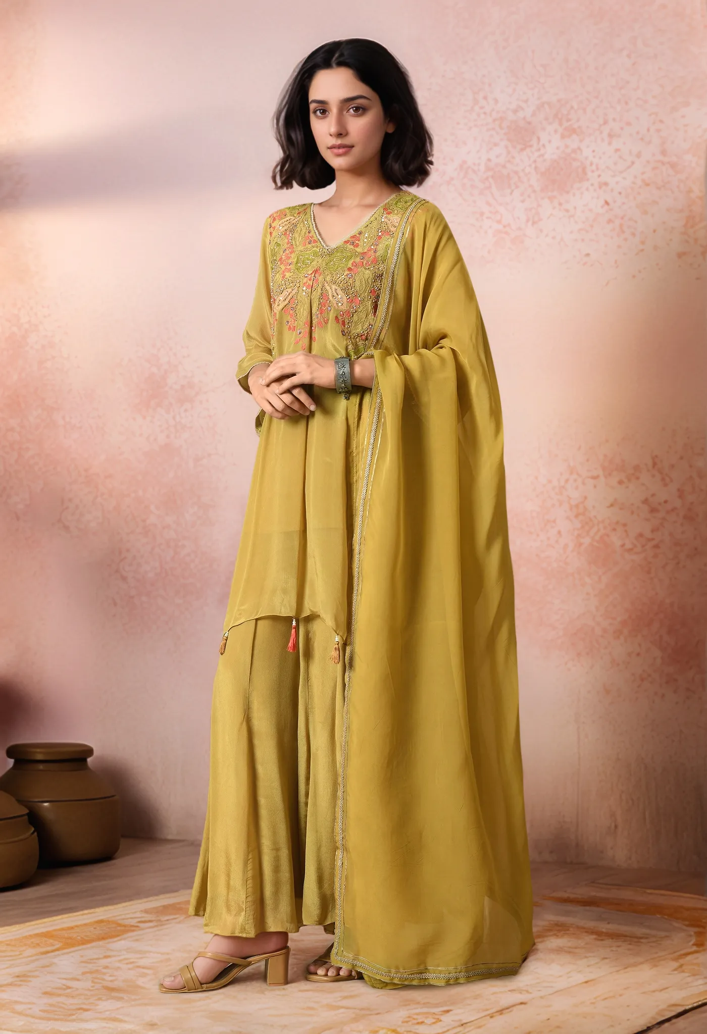 Mehendi green chinnon embroidered sharara set with asymmetric kurta, detailed yoke embroidery, tassel accents, matching sharara, and organza dupatta, offering contemporary festive elegance, Golden Muslin by Jhambthreads.