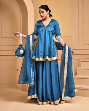 Teal Blue satin silk lehenga set with short kurta featuring V-neckline and gota lace detailing, flowing satin silk lehenga, organza dupatta with gota lace, and coordinating potli in Golden Muslin by Priyanka Rathore