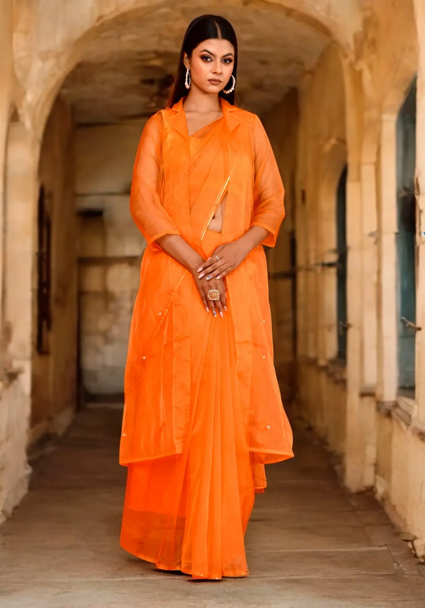 An elegant pastel orange organza saree with a subtle sheen and fluid drape from Golden Muslin by Priyanka Rathore, perfect for contemporary festive dressing.