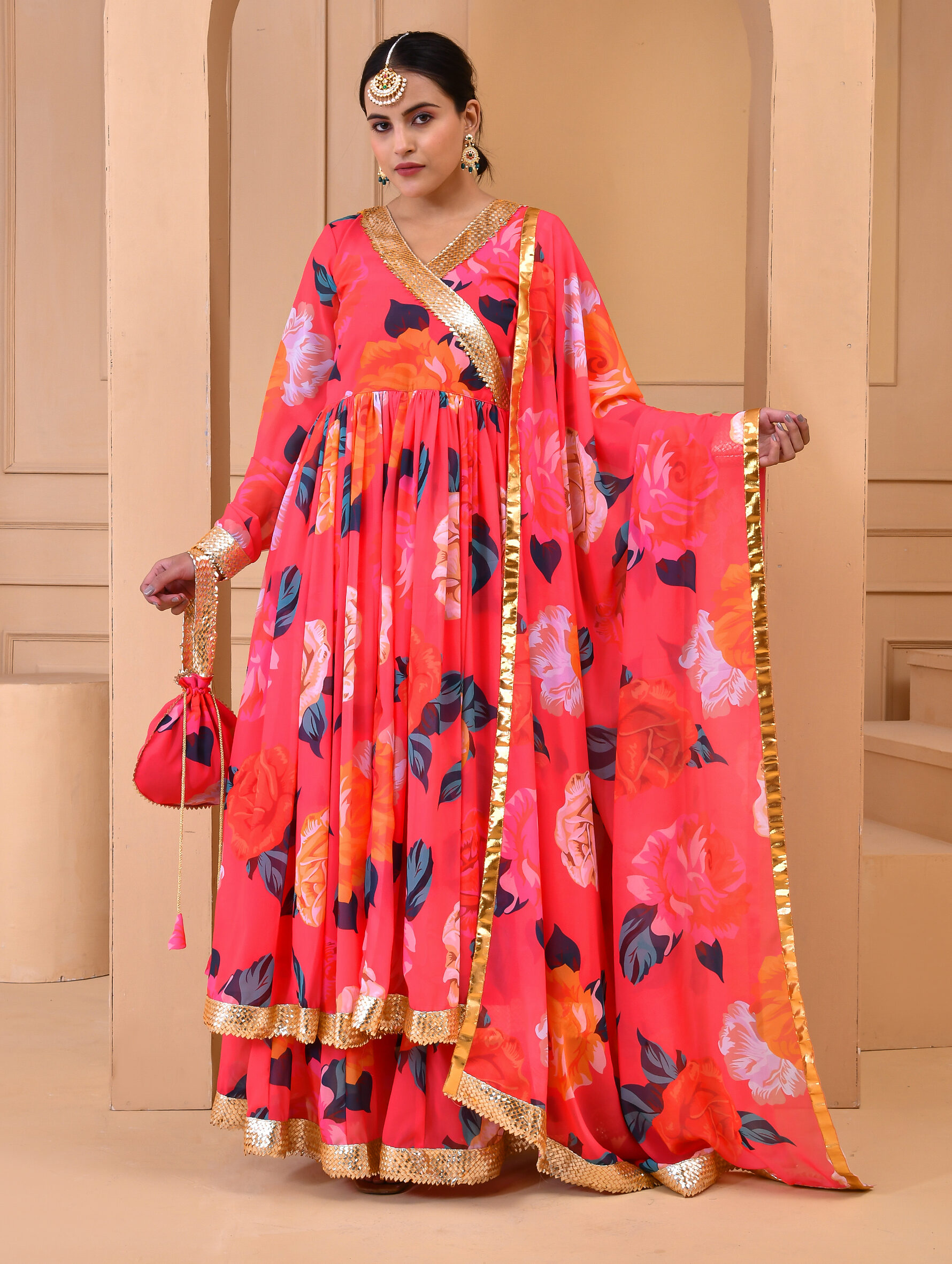 Coral georgette floral print sharara set with flared angrakha-style kurta featuring gota detailing, matching sharara, coordinated dupatta, and complementary potli in Golden Muslin by Priyanka Rathore