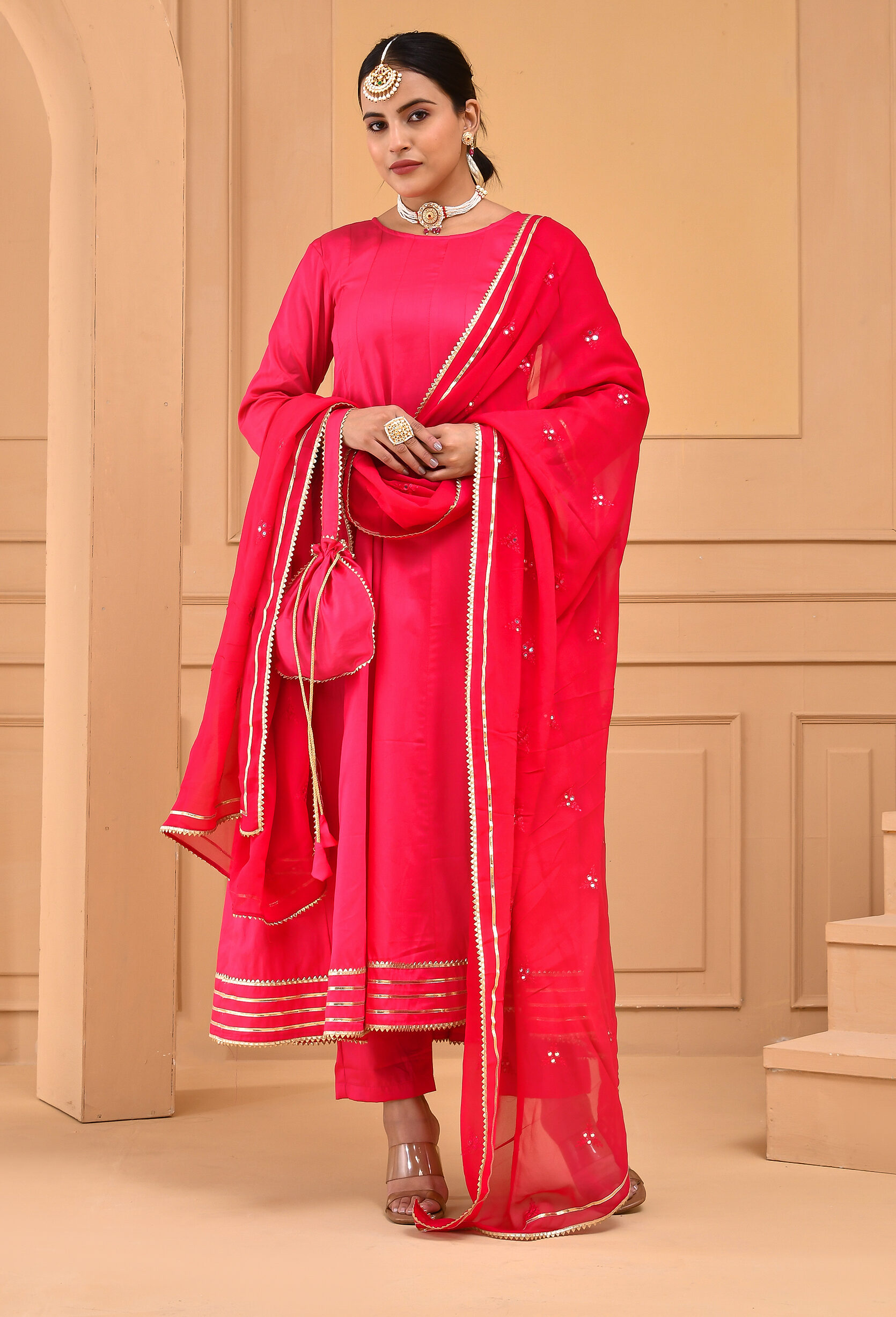 Ruby pink cotton silk Anarkali set by Golden Muslin by Priyanka Rathore featuring long kali-pattern kurta with gota lace detailing, matching pants, georgette dupatta with mirror work, and coordinated potli bag