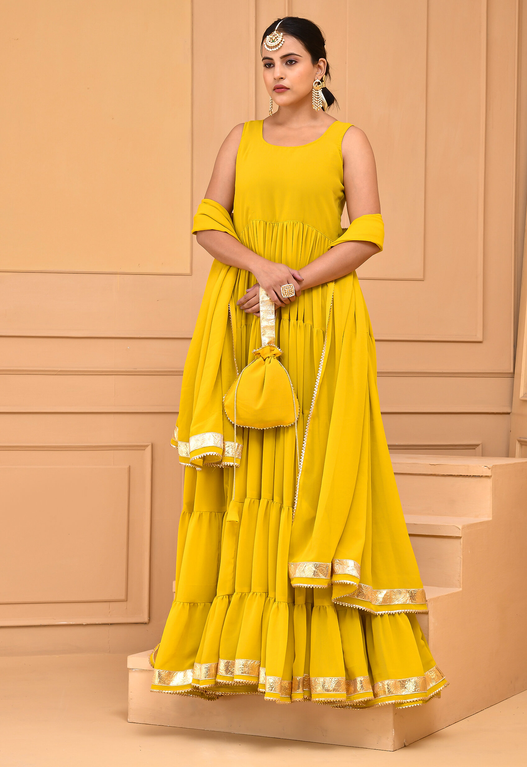 Yellow georgette Anarkali set by Golden Muslin by Priyanka Rathore featuring a flared tiered silhouette with gota detailing, paired with matching dupatta and potli