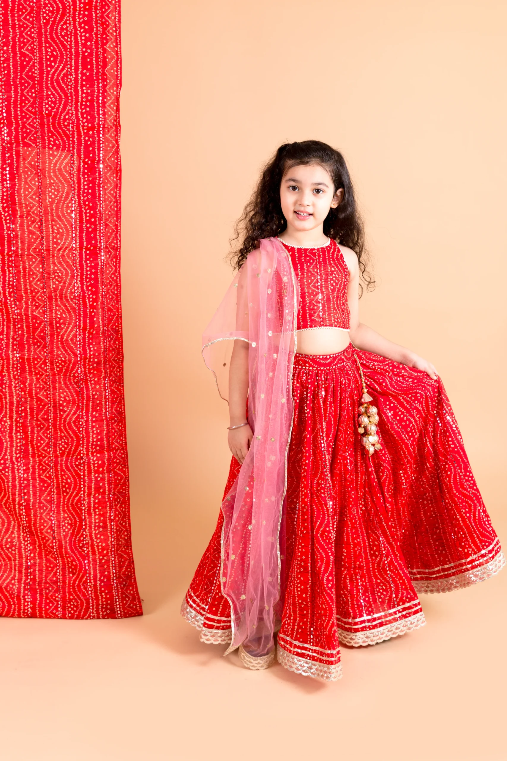 Red Bandhani Lehenga Set with mirror work crop top and net dupatta from Golden Muslin By Choti Buti