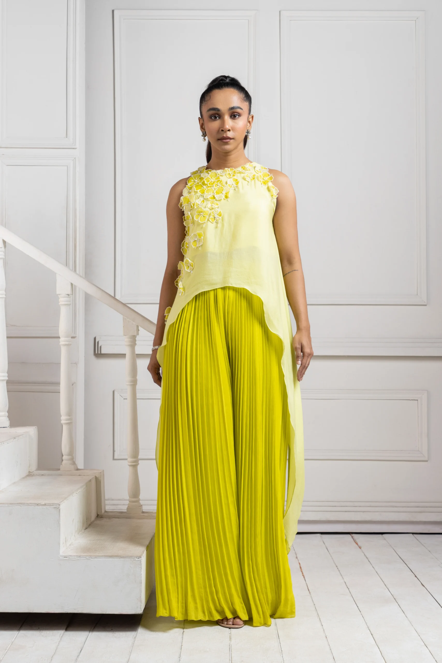 Model wearing yellow golden muslin asymmetric chiffon cape with lemon green pleated cascade pants