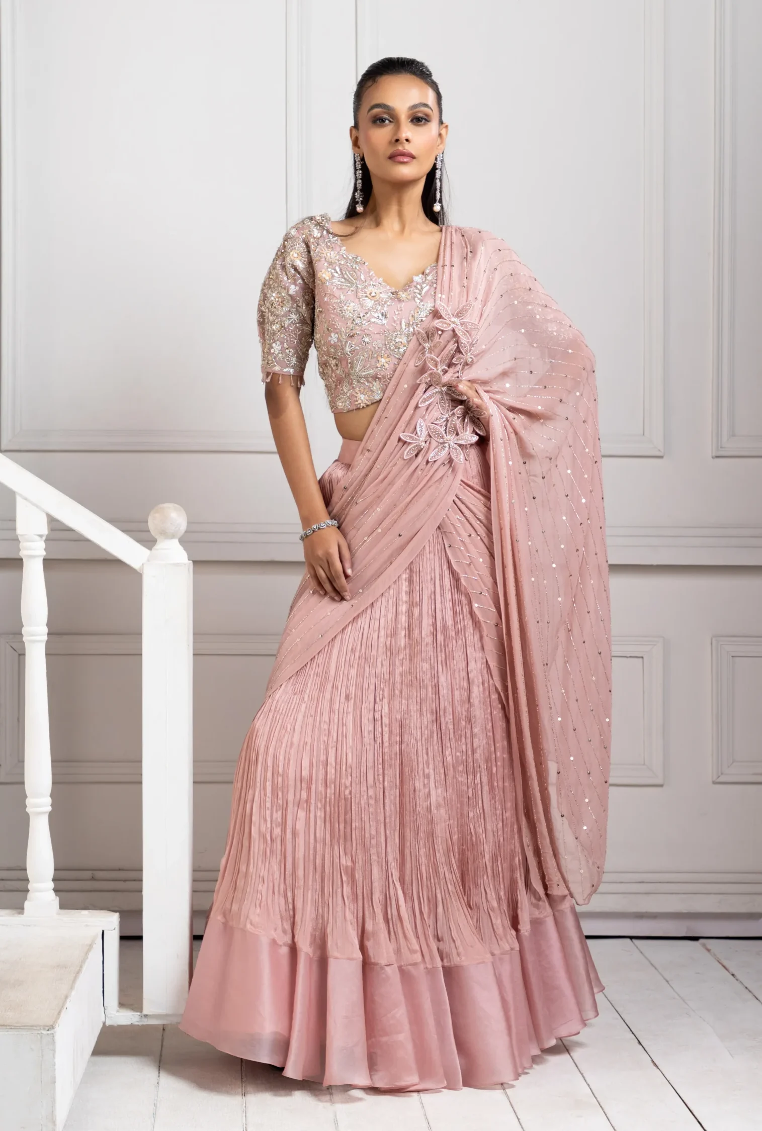 Model wearing blush rose golden muslin ruffled saree set with hand embroidered blouse and tiered hem